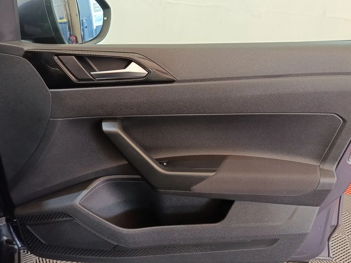 Vue rapprochée de la porte côté conducteur du Volkswagen Taigo gris foncé, avec poignée et panneau de commande des vitres.