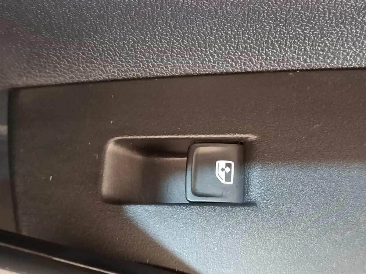 Gros plan sur le bouton de commande de lève-vitre arrière droit dans l'habitacle d'un Volkswagen Taigo gris foncé.