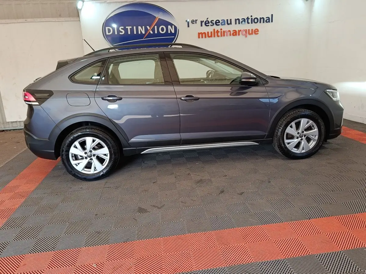 Vue de profil côté gauche d’un Volkswagen Taigo gris foncé 2023 garé en intérieur sur sol à damiers rouges et gris.