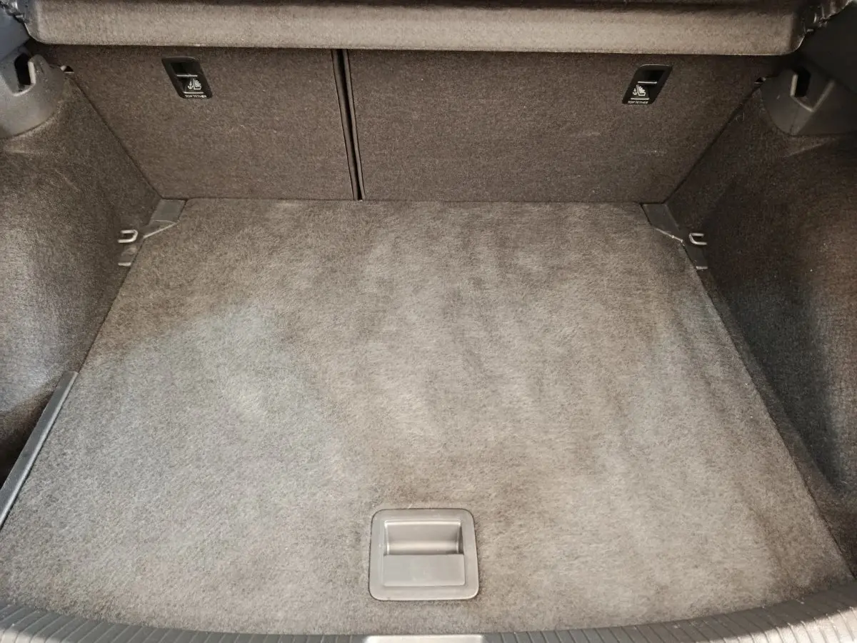 Coffre spacieux et vide du Volkswagen Taigo gris foncé, avec revêtement en tissu et poignées de fixation visibles.