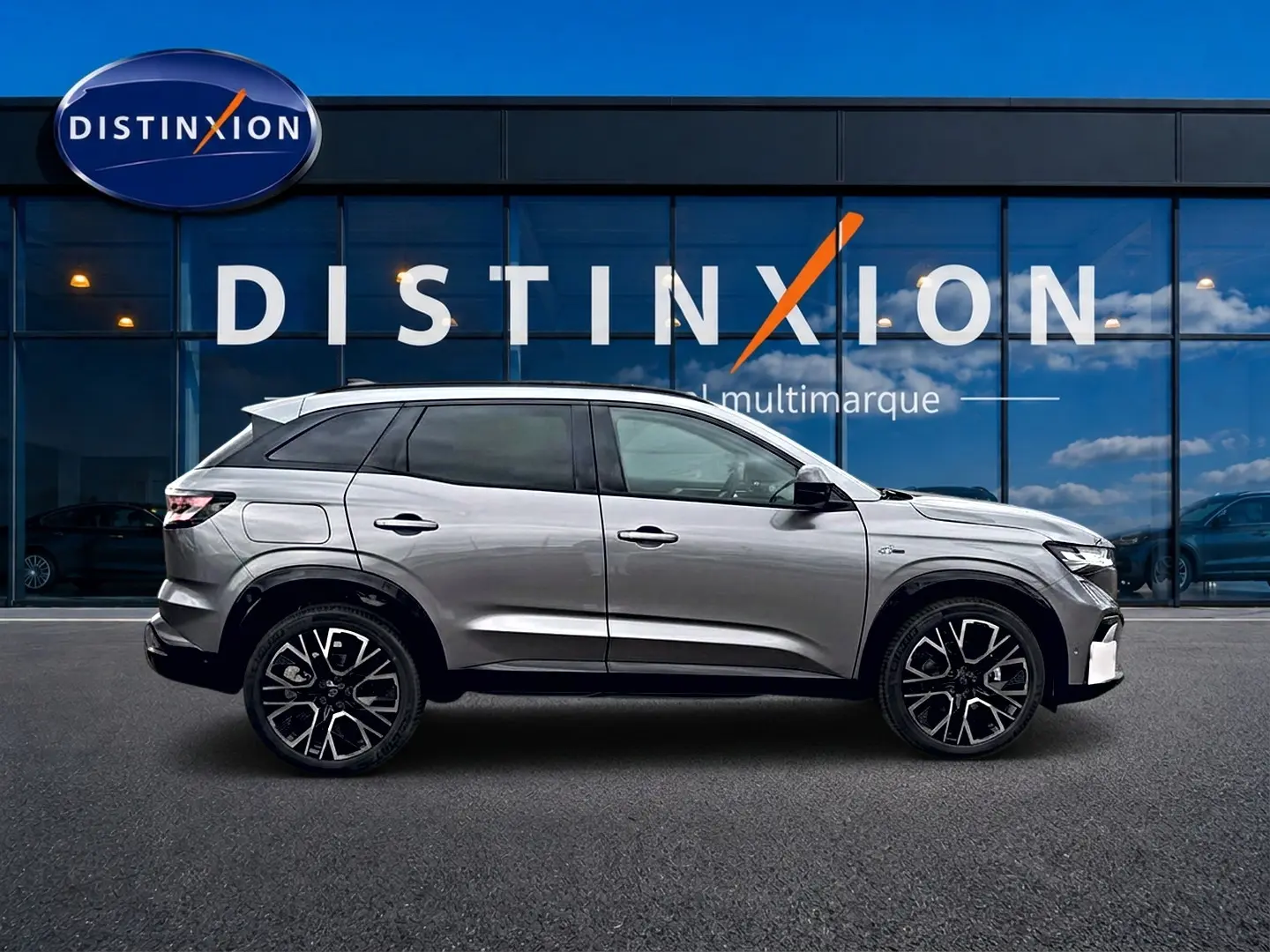 Profil droit du Renault Austral gris schiste avec jantes alu noires, devant une vitrine bleue Distinxion multimarque.