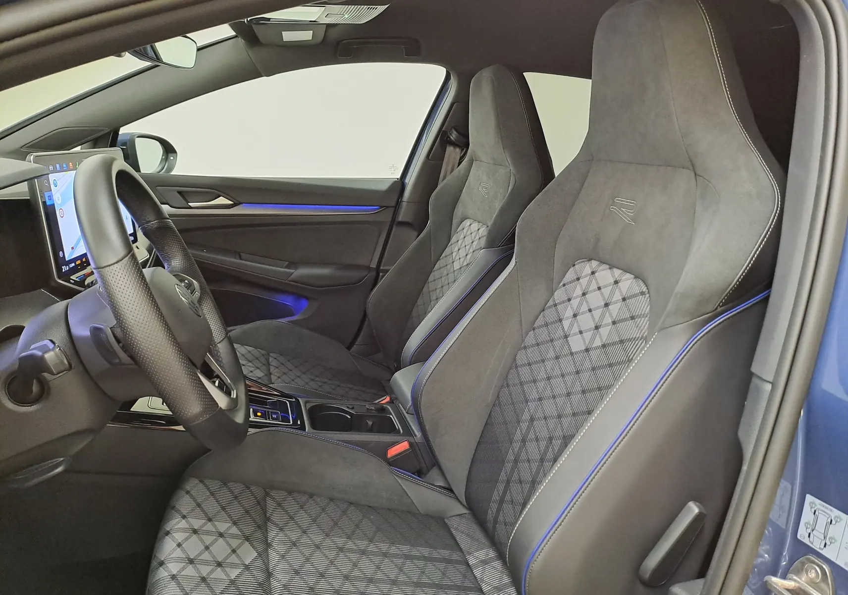 Vue intérieure côté conducteur de la Volkswagen Golf 1.5 eTSI R-Line 2025 avec sièges sport en tissu gris à surpiqûres bleues.