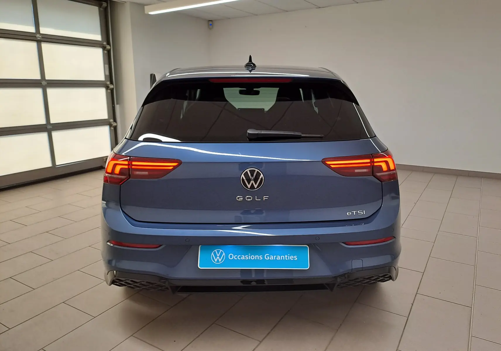Vue arrière d'une Volkswagen Golf 1.5 eTSI 150 DSG7 R-Line Edition bleu Anémone avec feux allumés en intérieur.