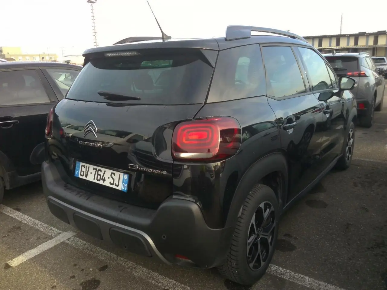 Vue 3/4 arrière droite d'un Citroën C3 Aircross noir avec jantes alliage diamantées et barres de toit noires.