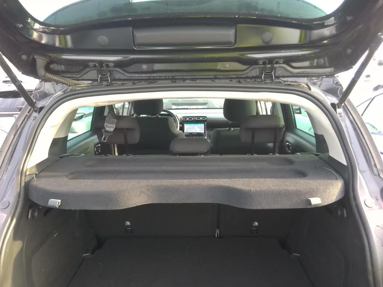 Vue arrière ouverte du coffre d'une Citroën C3 Aircross noire avec tablette cache-bagages et sièges arrière visibles.