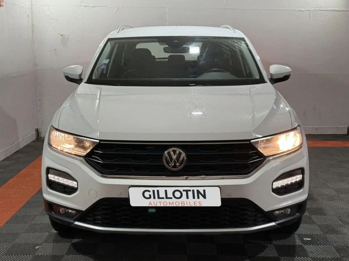 Volkswagen T-Roc blanc vue de face avec phares allumés et calandre noire dans un garage.
