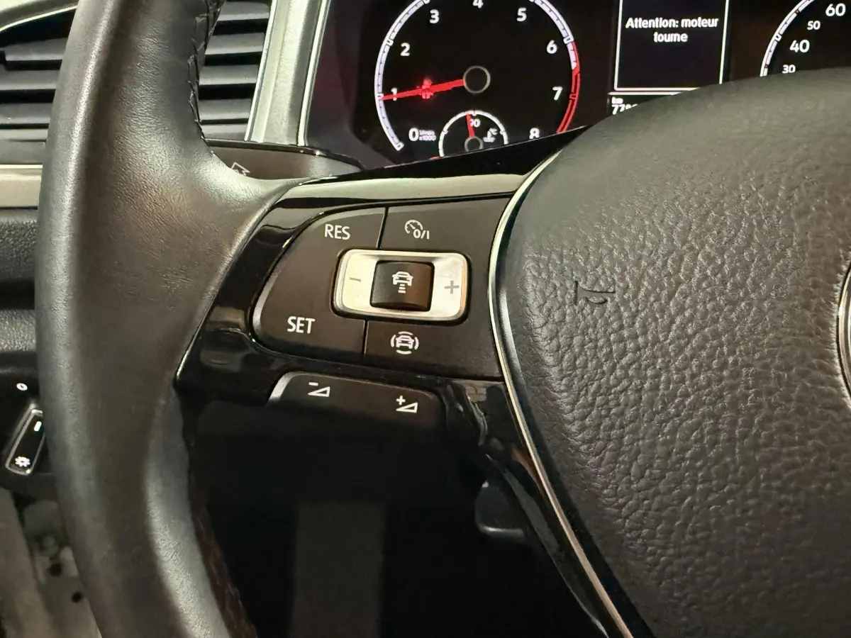 Gros plan sur le volant cuir noir du Volkswagen T-Roc 2020, avec commandes de régulateur adaptatif et tableau de bord numérique visible.