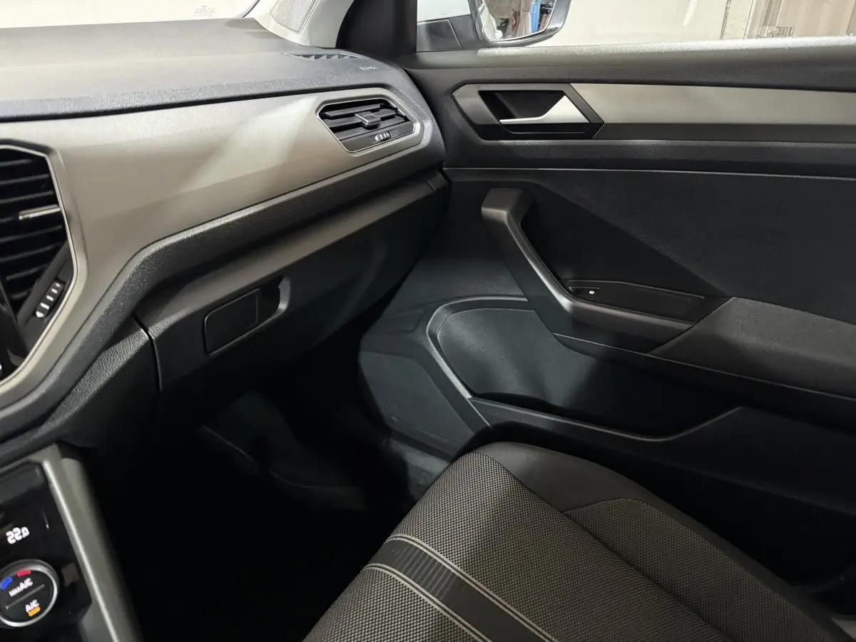 Intérieur côté passager du Volkswagen T-Roc blanc 2020, montrant la porte, tableau de bord et siège tissu gris.