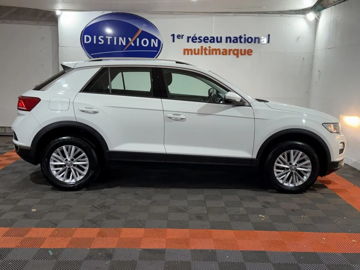 Profil côté gauche d'un Volkswagen T-Roc blanc 2020 garé en intérieur sur sol à damiers noir et orange.