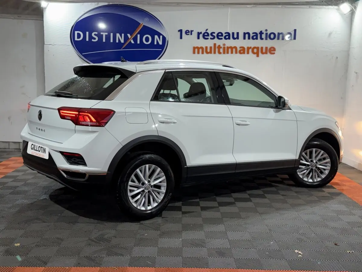Vue 3/4 arrière droite d'un Volkswagen T-Roc blanc 2020 en intérieur avec jantes alliage et feux LED allumés.