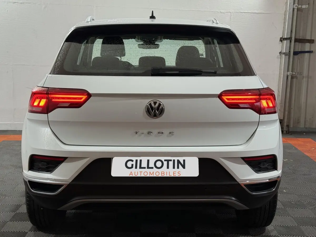 Vue arrière d'un Volkswagen T-Roc blanc 2020 avec feux LED allumés et logo visible sur un fond intérieur neutre.