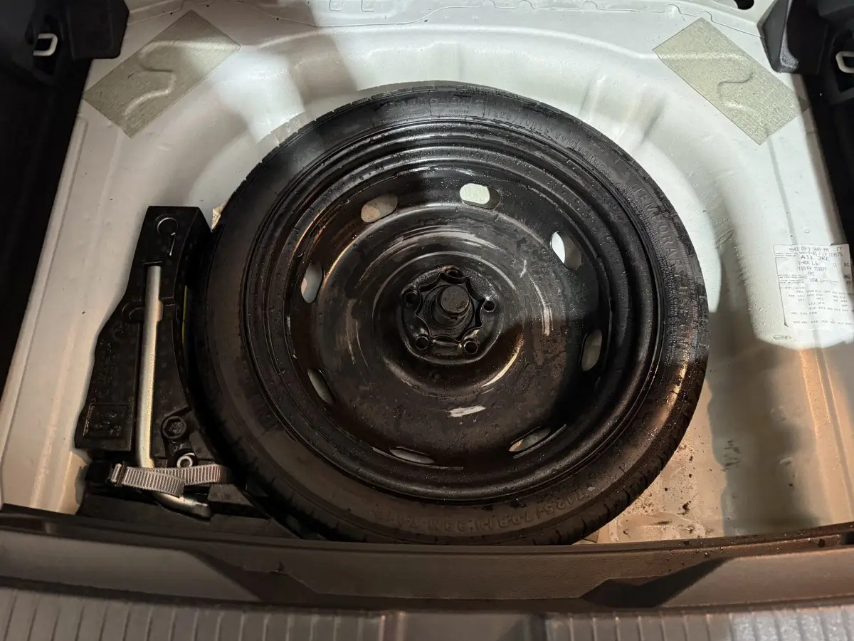 Roue de secours noire dans le coffre blanc d'un Volkswagen T-Roc 2020, avec outils de changement visibles.