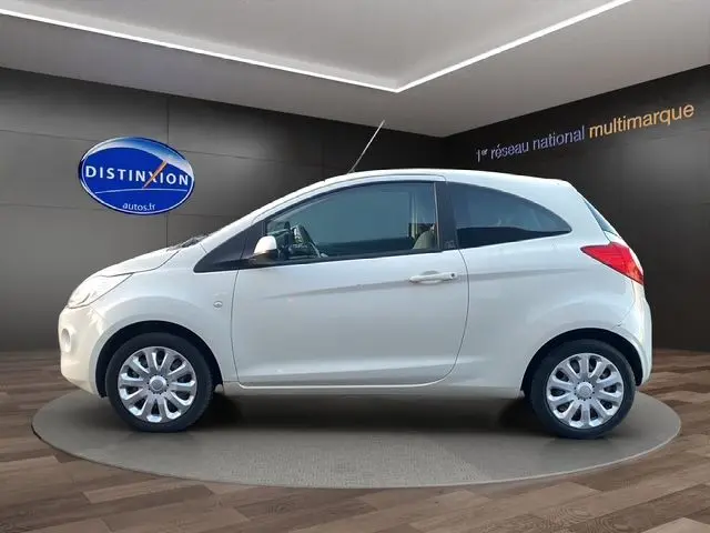 Vue de profil côté gauche d'une Ford KA blanche de 2015, compacte et épurée, sur fond intérieur showroom.
