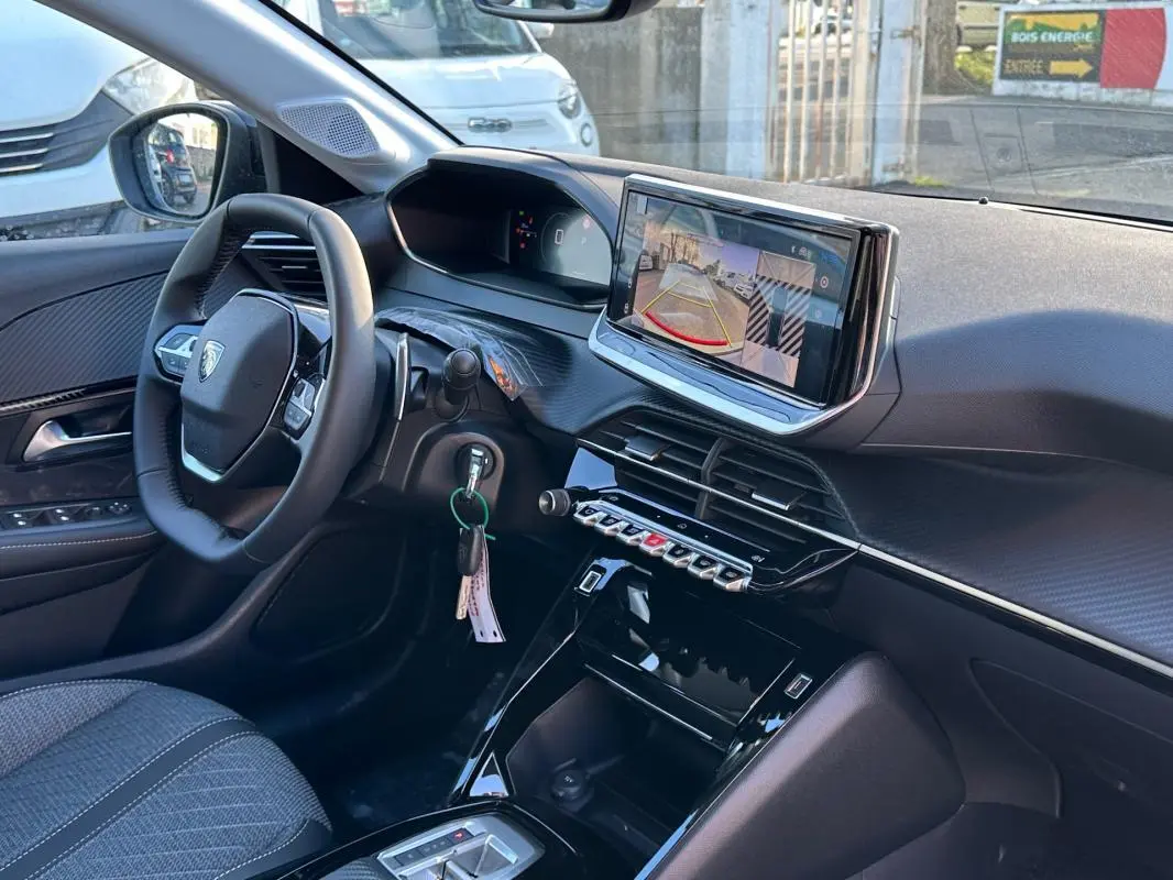 Vue intérieure côté conducteur du Peugeot 208 Hybrid blanc 2025, avec écran tactile affichant la caméra de recul et volant multifonction.
