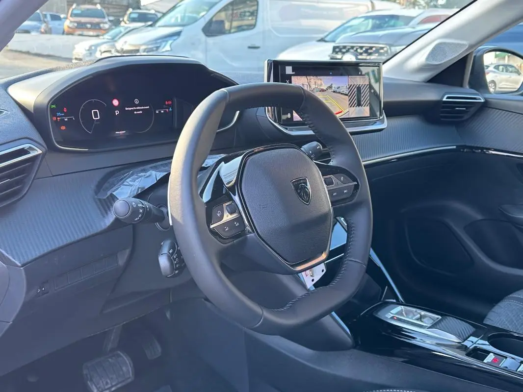 Vue intérieure du poste de conduite de la Peugeot 208 Hybrid 110 e-DCS6 Allure 2025, avec volant multifonction et écran tactile.