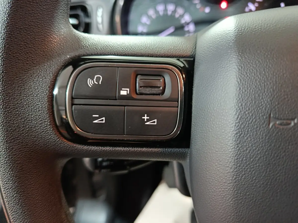 Gros plan sur les commandes multifonctions à gauche du volant gris foncé du Citroën C3 BlueHDi 2024.
