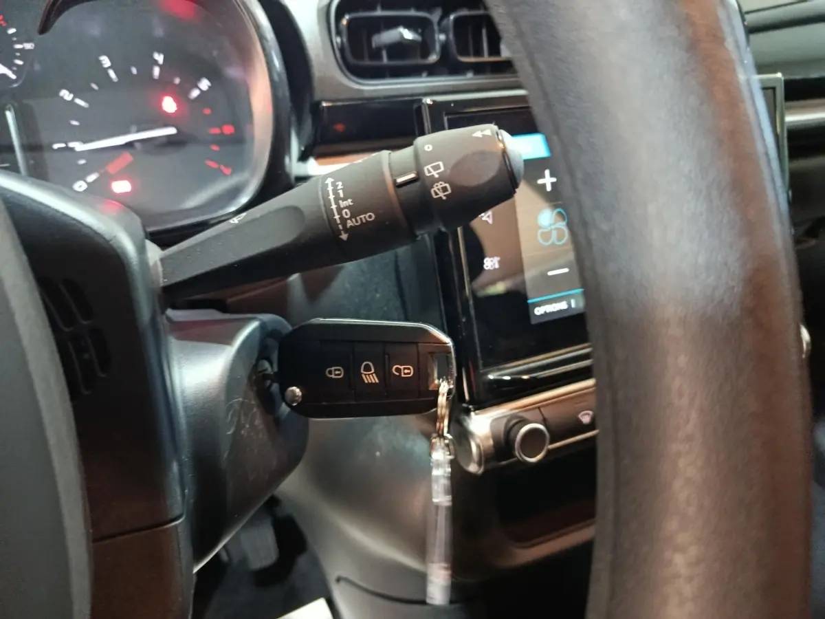 Gros plan sur le volant et la clé de contact d'une Citroën C3 gris foncé, avec tableau de bord tactile en arrière-plan.