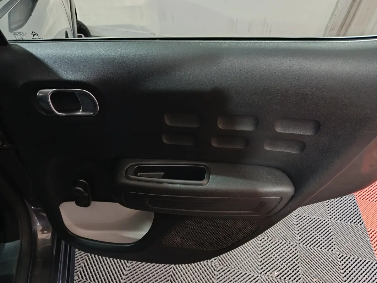 Vue intérieure de la porte côté conducteur de la Citroën C3 gris foncé, avec poignée intégrée et motifs rectangulaires.
