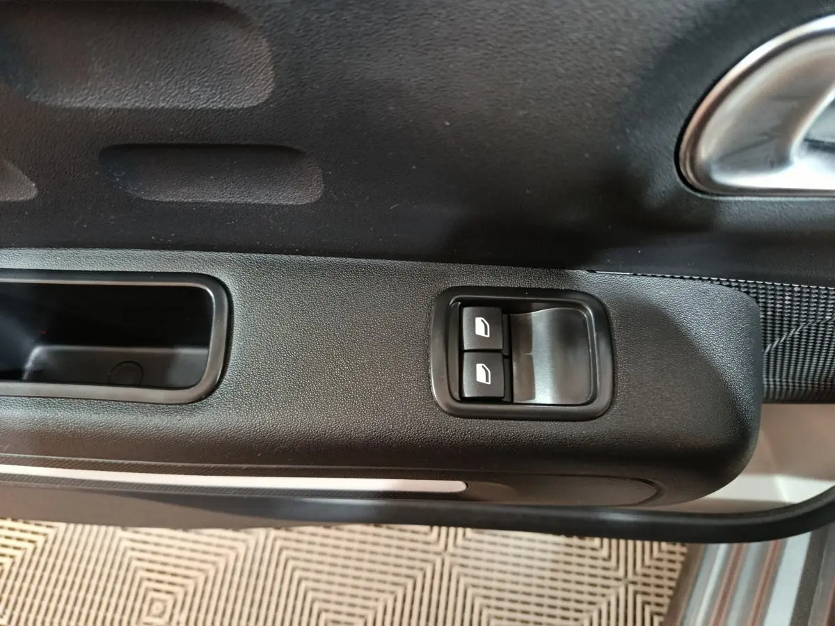 Gros plan sur les commandes des vitres électriques sur la porte côté conducteur d'une Citroën C3 gris foncé 2024.