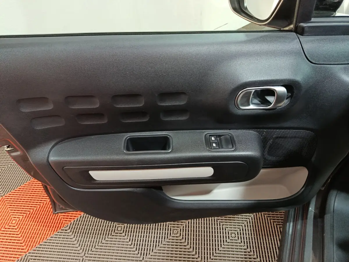 Gros plan sur la porte intérieure côté conducteur de la Citroën C3 gris foncé, avec poignée argentée et commandes de vitres.