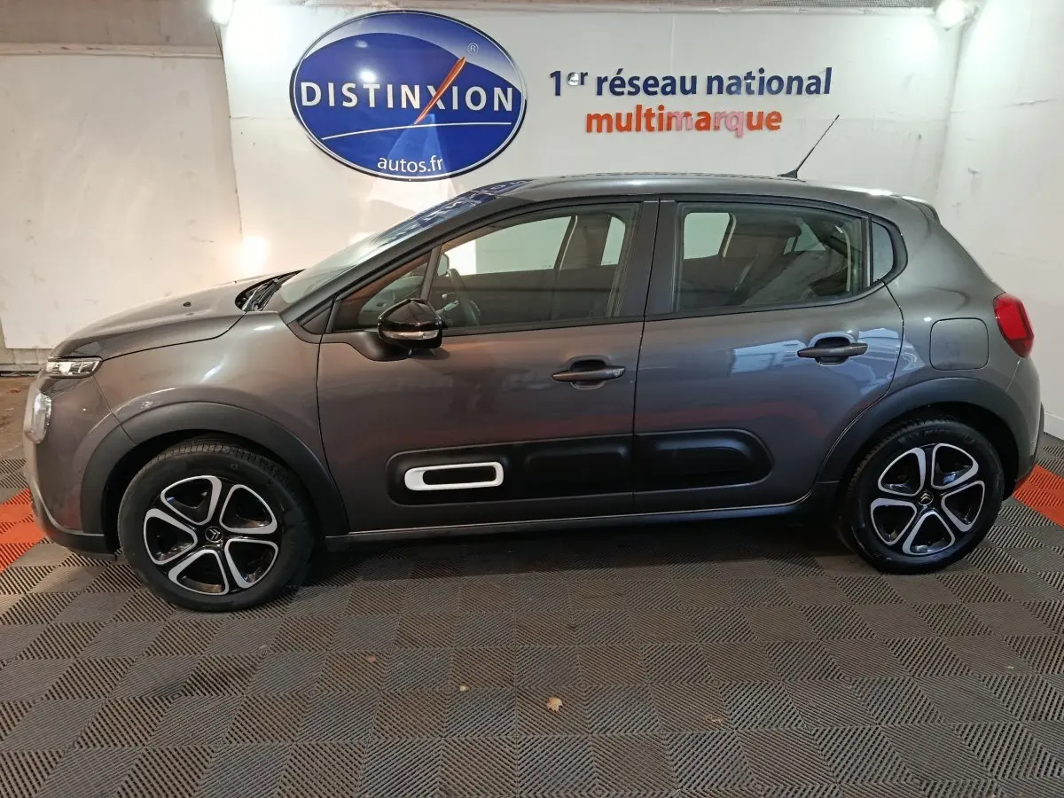 Vue de profil côté gauche d'une Citroën C3 gris foncé 2024 avec jantes alliage et protections latérales noires.