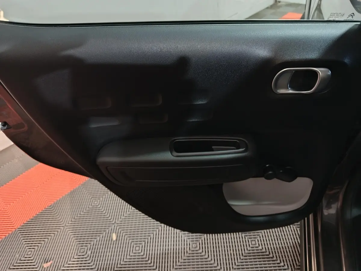 Vue intérieure de la porte arrière droite d'une Citroën C3 gris foncé, avec poignée et manivelle de vitre.