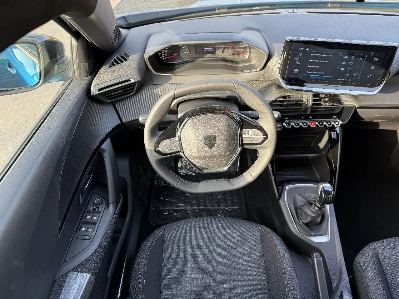 Vue intérieure du poste de conduite du Peugeot 2008 2025 bleu obsession, avec volant compact et boîte manuelle visible.