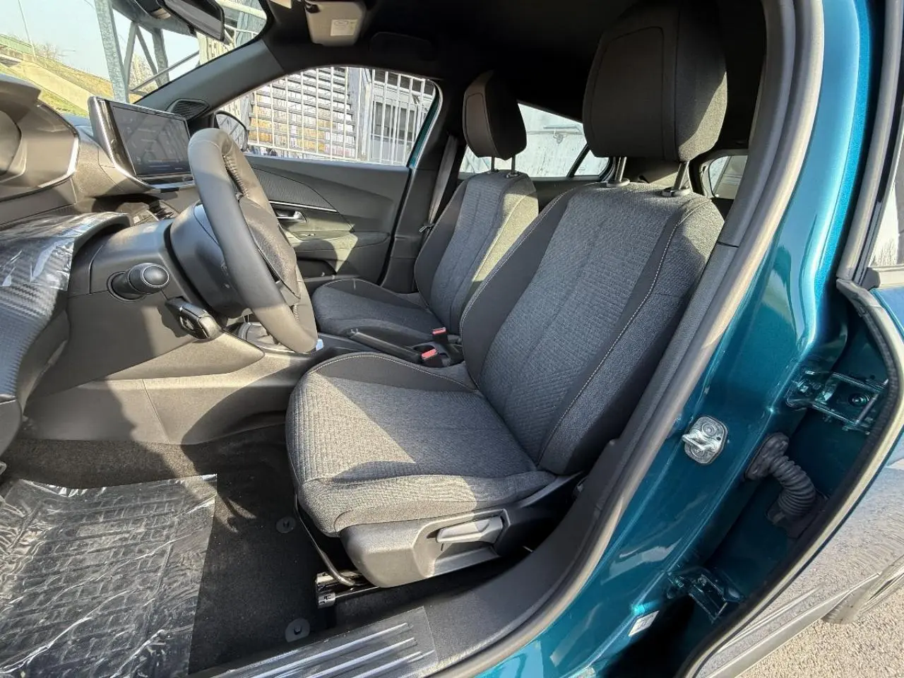 Vue intérieure côté conducteur du Peugeot 2008 2025 bleu obsession, montrant les sièges avant en tissu gris et le volant.