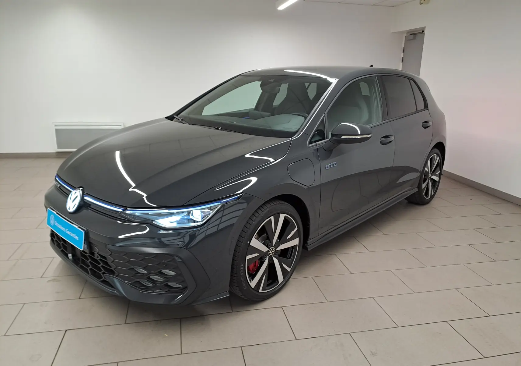 Volkswagen Golf 1.5 eHybrid 272 GTE gris Urano vue de face avec phares LED allumés en intérieur.
