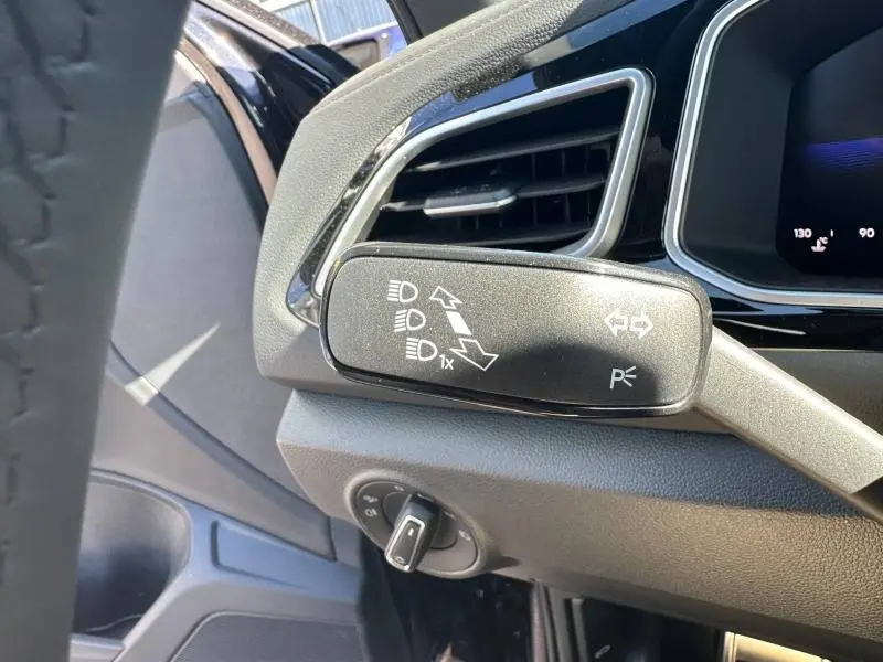 Gros plan sur la commande des feux et clignotants côté gauche du tableau de bord noir du Volkswagen T-Roc 2025.