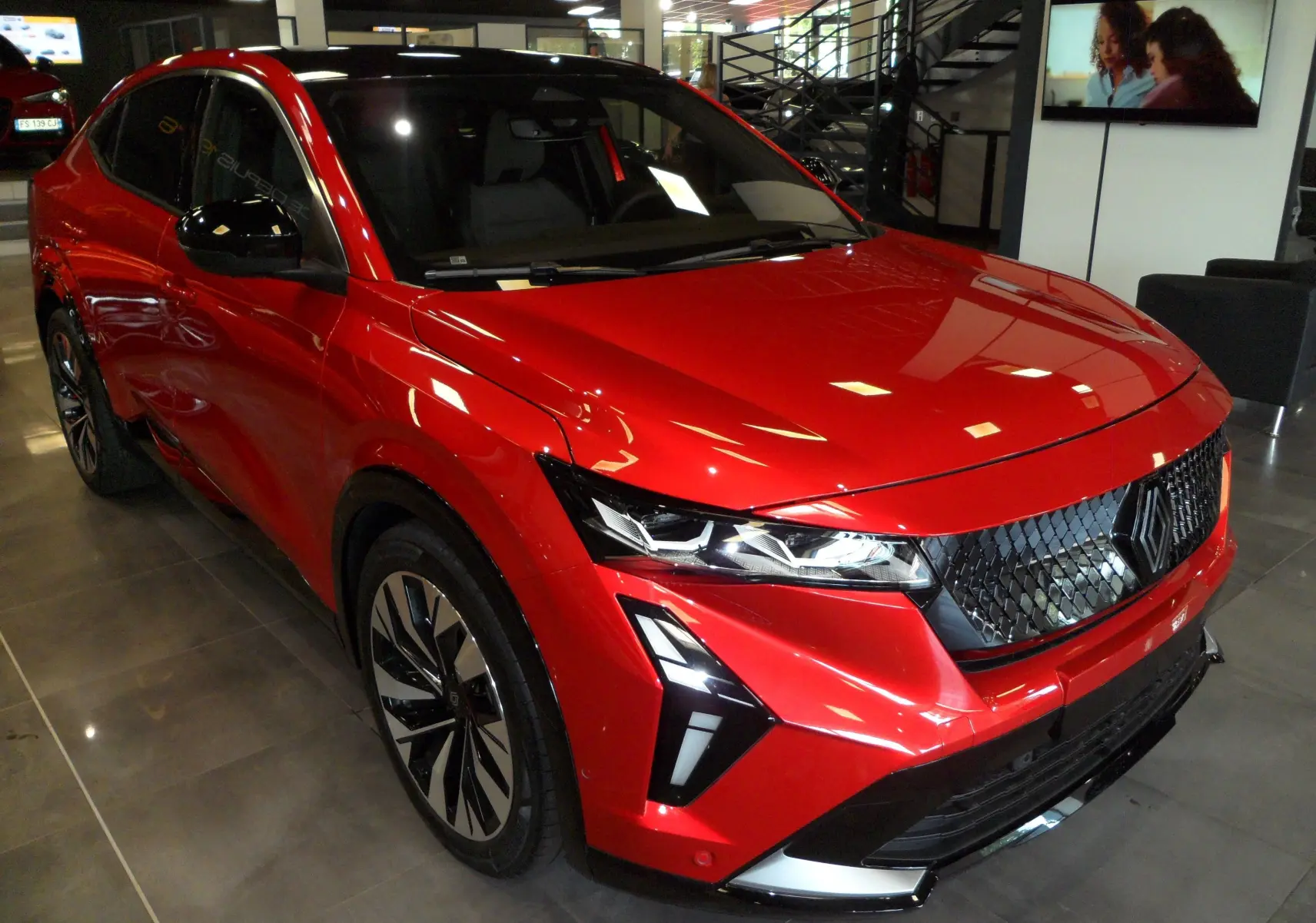 Renault Rafale E-Tech Full Hybrid rouge flamme avec toit noir, vue 3/4 avant en showroom, calandre noire distinctive.