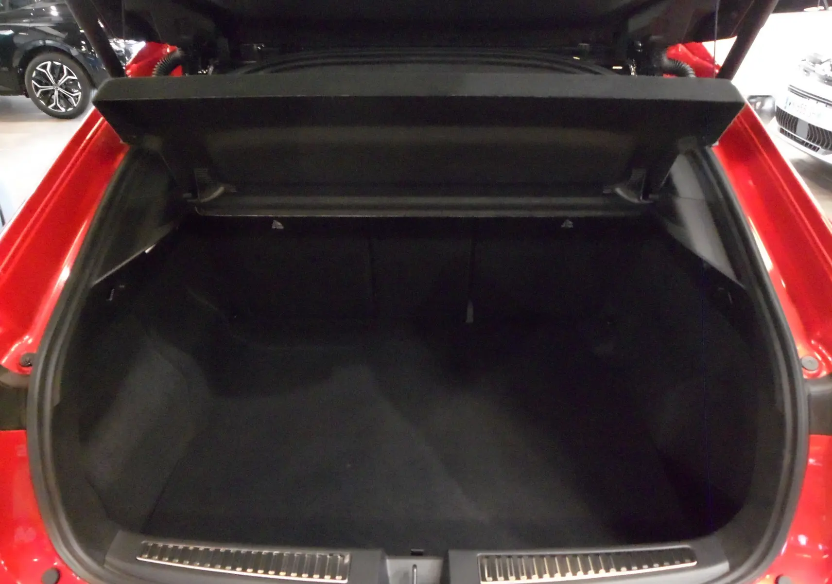 Coffre ouvert d'une Renault Rafale E-Tech Full Hybrid rouge flamme avec toit noir, vue arrière intérieure du coffre spacieux.