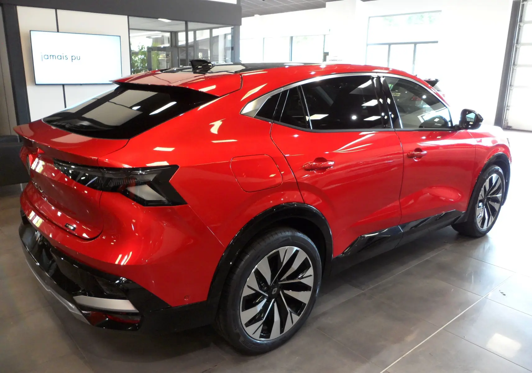 Vue 3/4 arrière droite d'une Renault Rafale E-Tech Full Hybrid rouge Flamme avec toit noir et jantes bi-ton en showroom.
