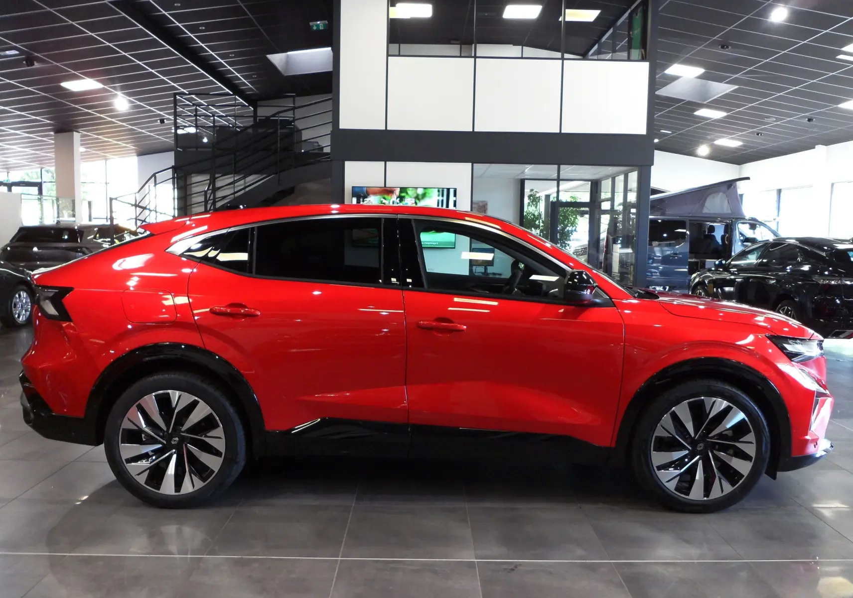 Profil latéral droit d'une Renault Rafale E-Tech Full Hybrid rouge Flamme avec toit noir et jantes biton dans un showroom.