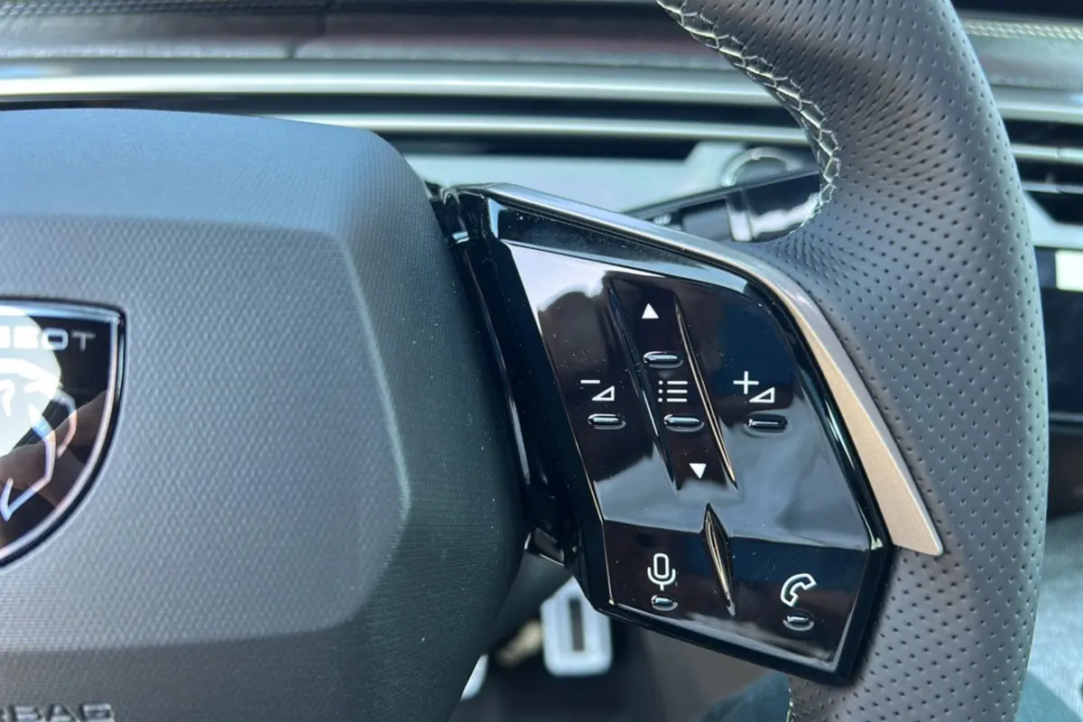 Gros plan sur les commandes à droite du volant perforé du Peugeot 3008 Hybrid 2025 gris titane avec logo lion.