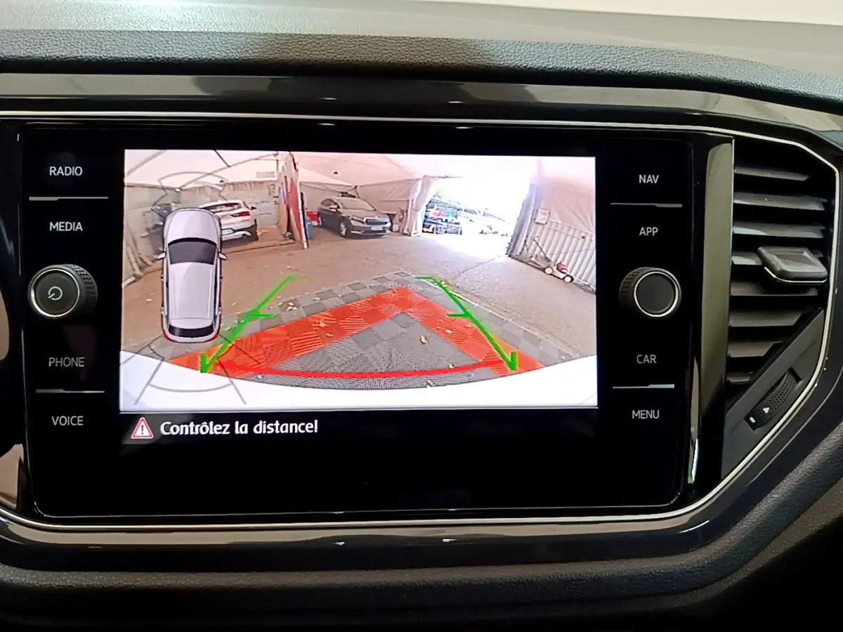 Écran tactile intérieur montrant la caméra de recul et l’aide au stationnement du Volkswagen T-Roc blanc.