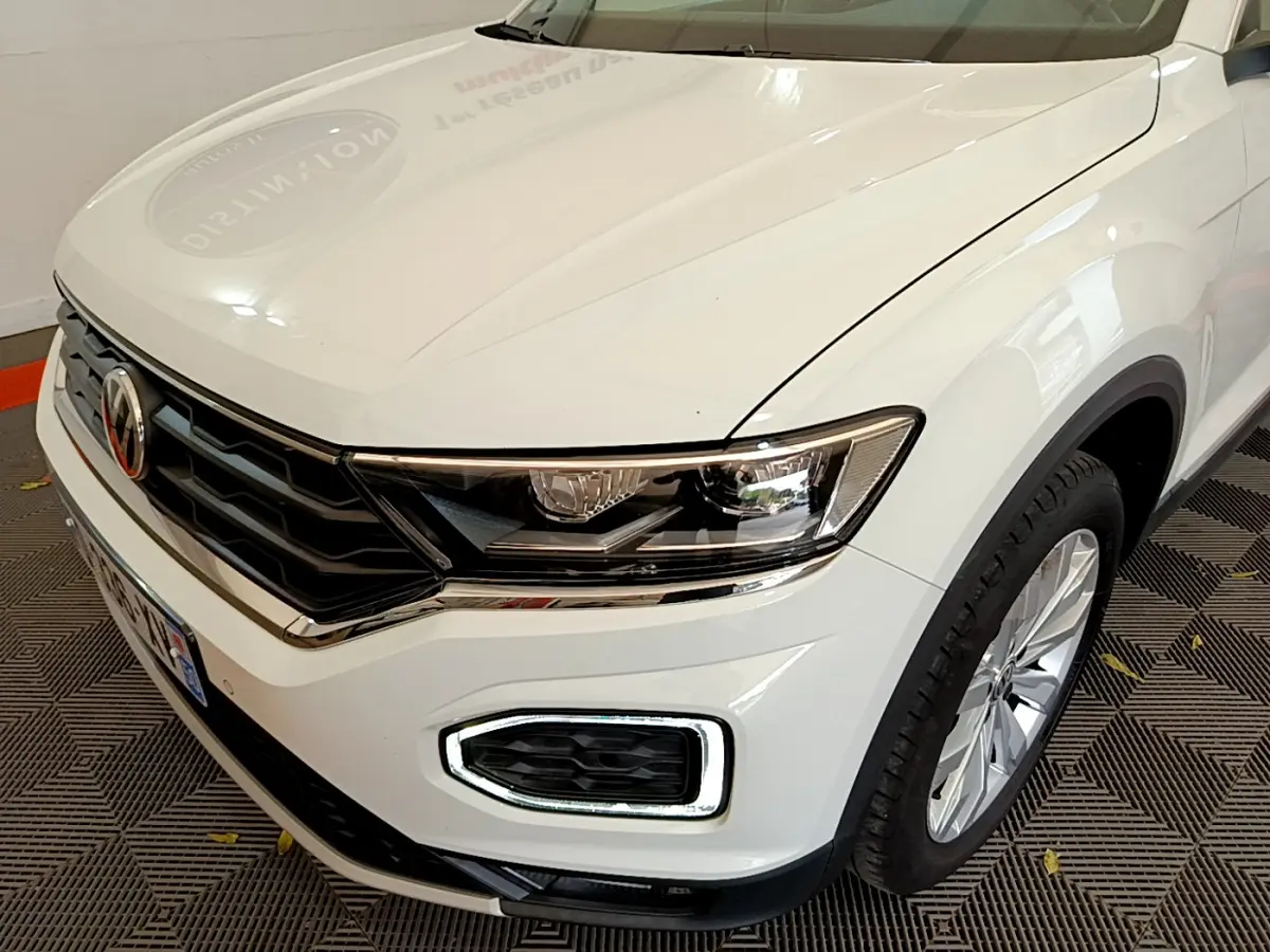 Vue 3/4 avant droit d'un Volkswagen T-Roc blanc avec feux LED et calandre noire chromée.