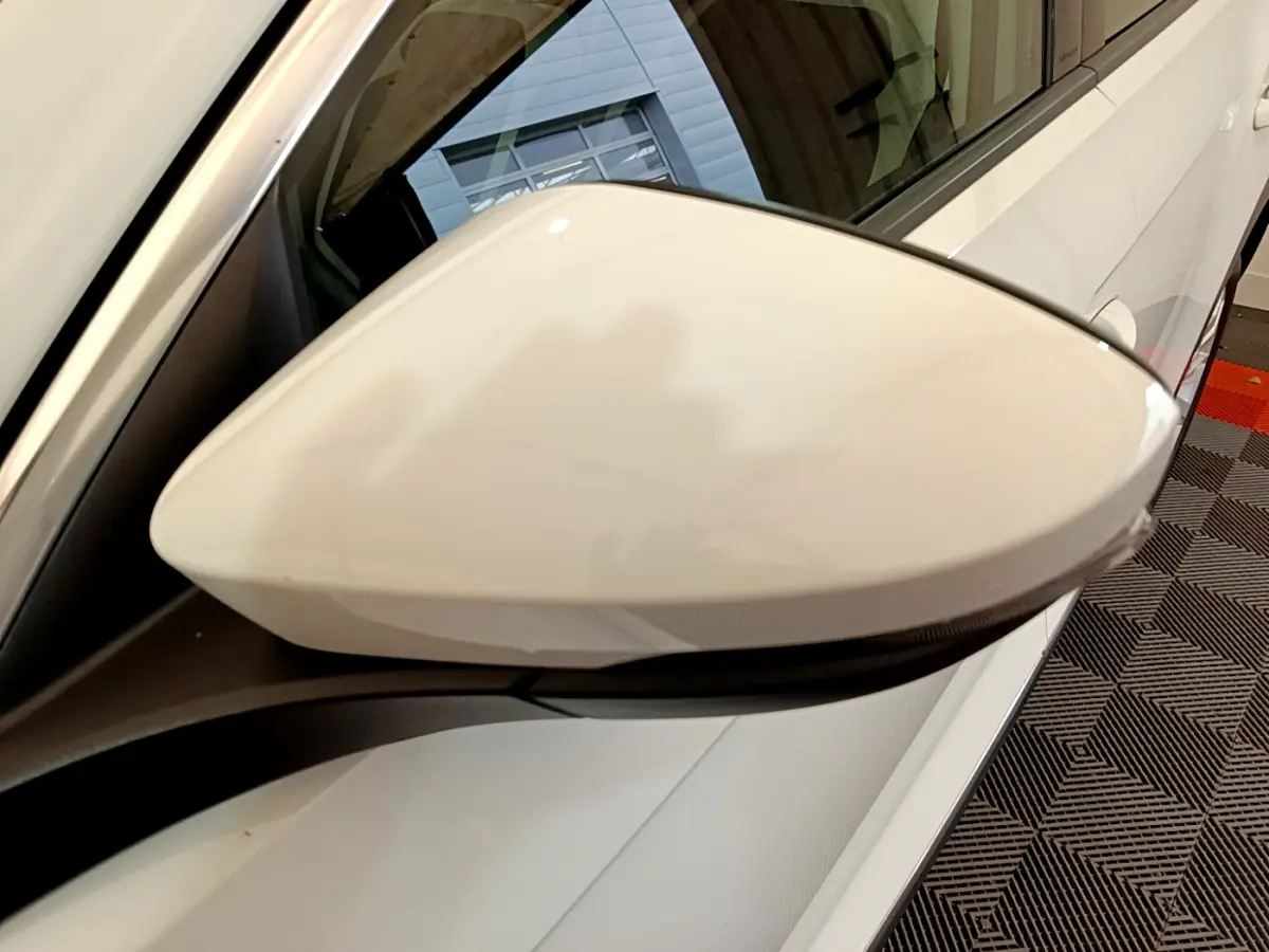 Rétroviseur côté gauche blanc du Volkswagen T-Roc 1.5 TSI 150 EVO CARAT DSG7 vu en gros plan avec carrosserie blanche.