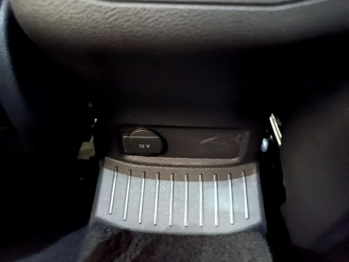 Prise 12V noire en gros plan sous la console centrale du Volkswagen T-Roc blanc, intérieur sombre.