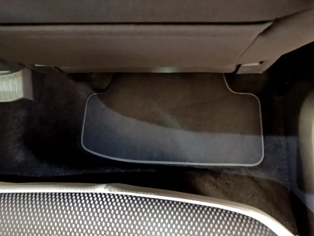 Vue du sol côté passager avant du Volkswagen T-Roc blanc, avec tapis de sol et partie inférieure du siège visible.