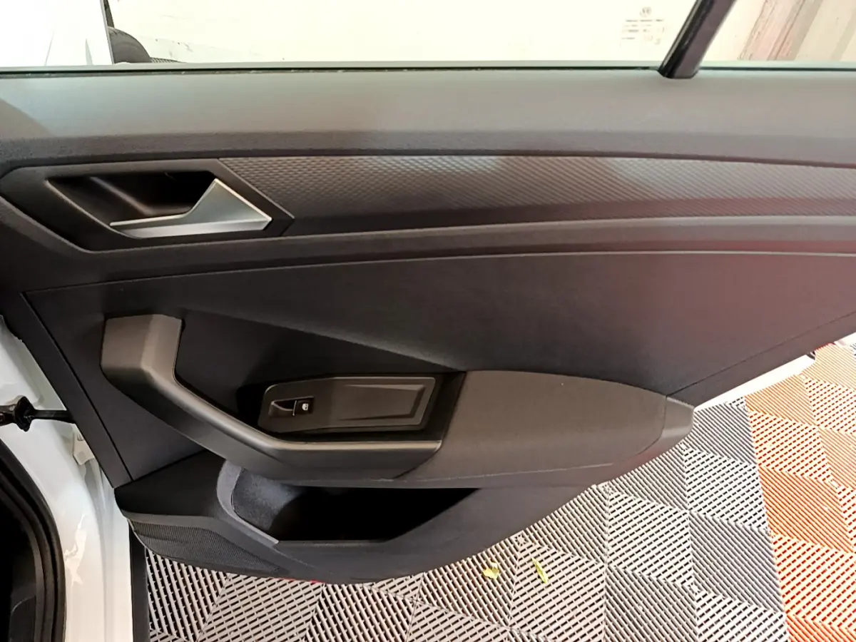 Vue intérieure du panneau de porte côté gauche d'un Volkswagen T-Roc blanc, avec poignée et commande de fenêtre noire.
