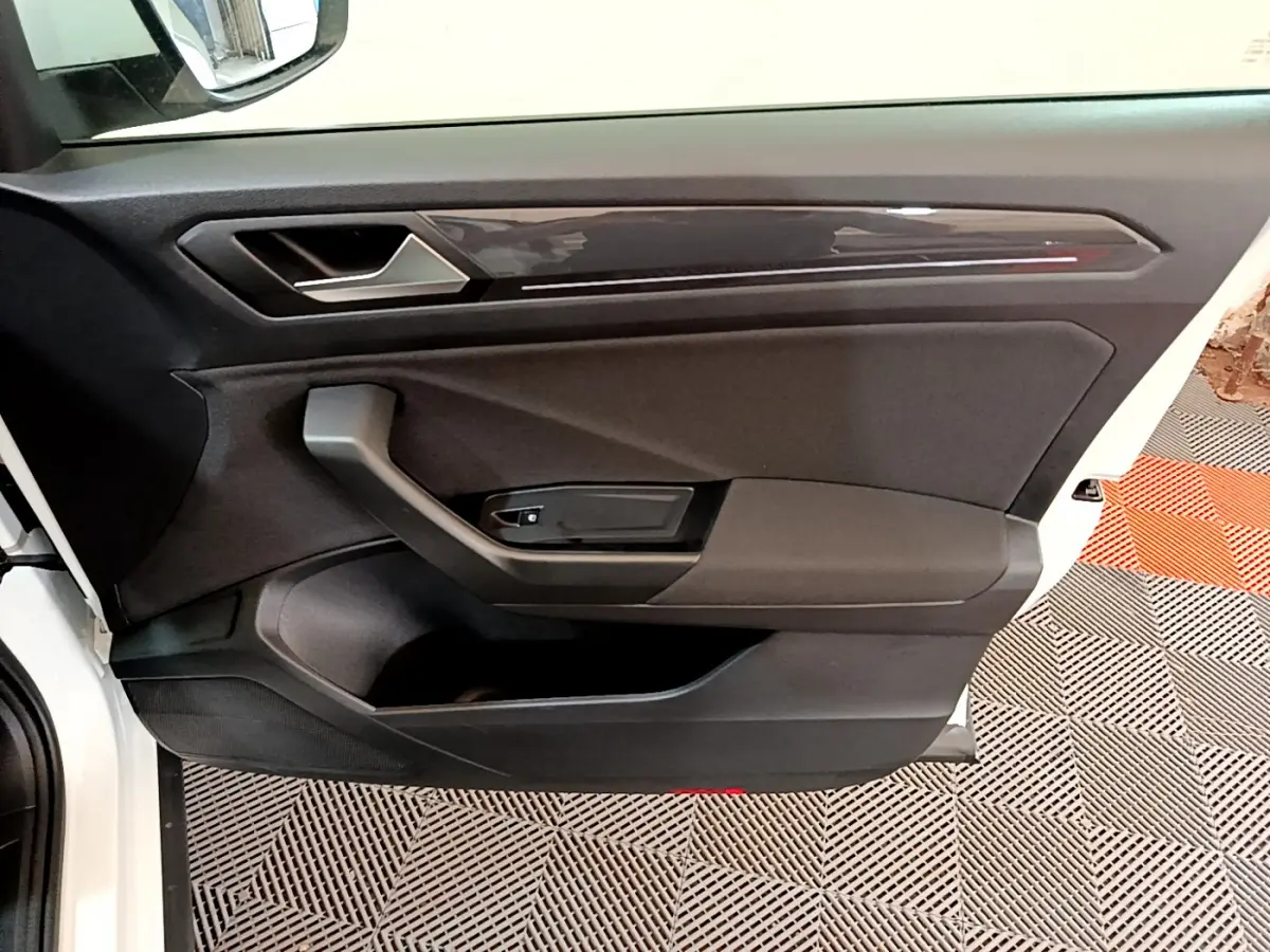 Vue rapprochée de la porte avant gauche noire du Volkswagen T-Roc blanc, avec poignée et panneau de commande.