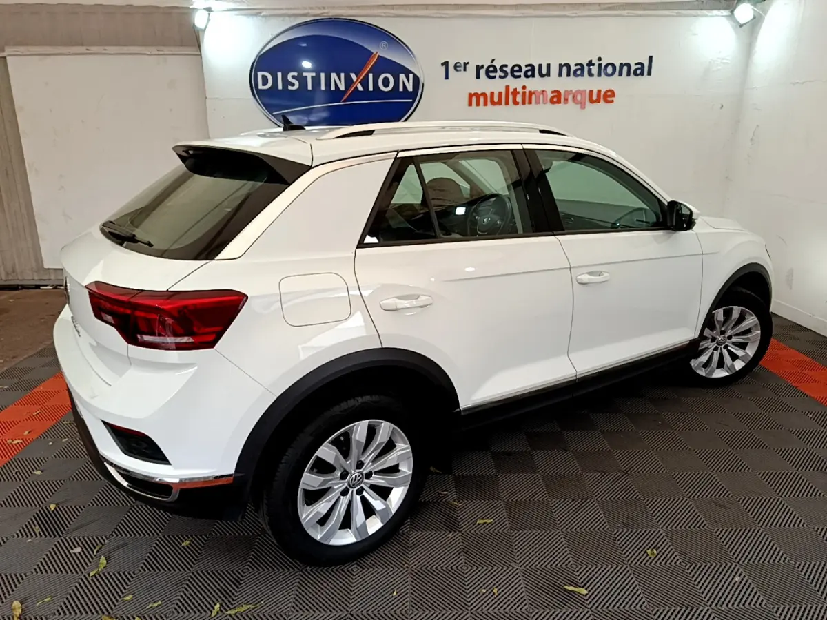 Volkswagen T-Roc blanc vue 3/4 arrière droit en intérieur, avec jantes alliage et toit ouvrant noir.
