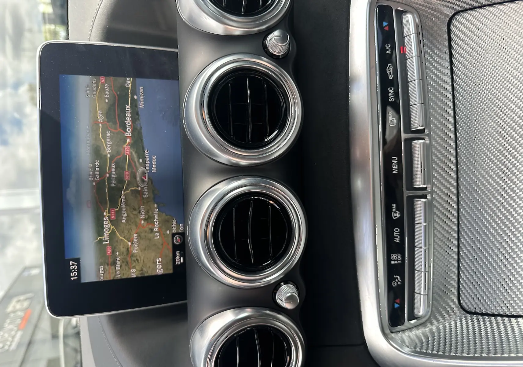 Vue rapprochée du tableau de bord d'une Mercedes AMG GT 2015 gris foncé, avec écran GPS et aérateurs ronds chromés.