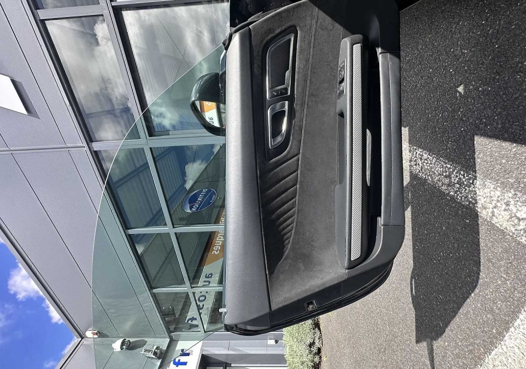 Portière côté gauche ouverte d'une Mercedes AMG GT gris foncé, montrant l'intérieur en alcantara et inserts carbone.