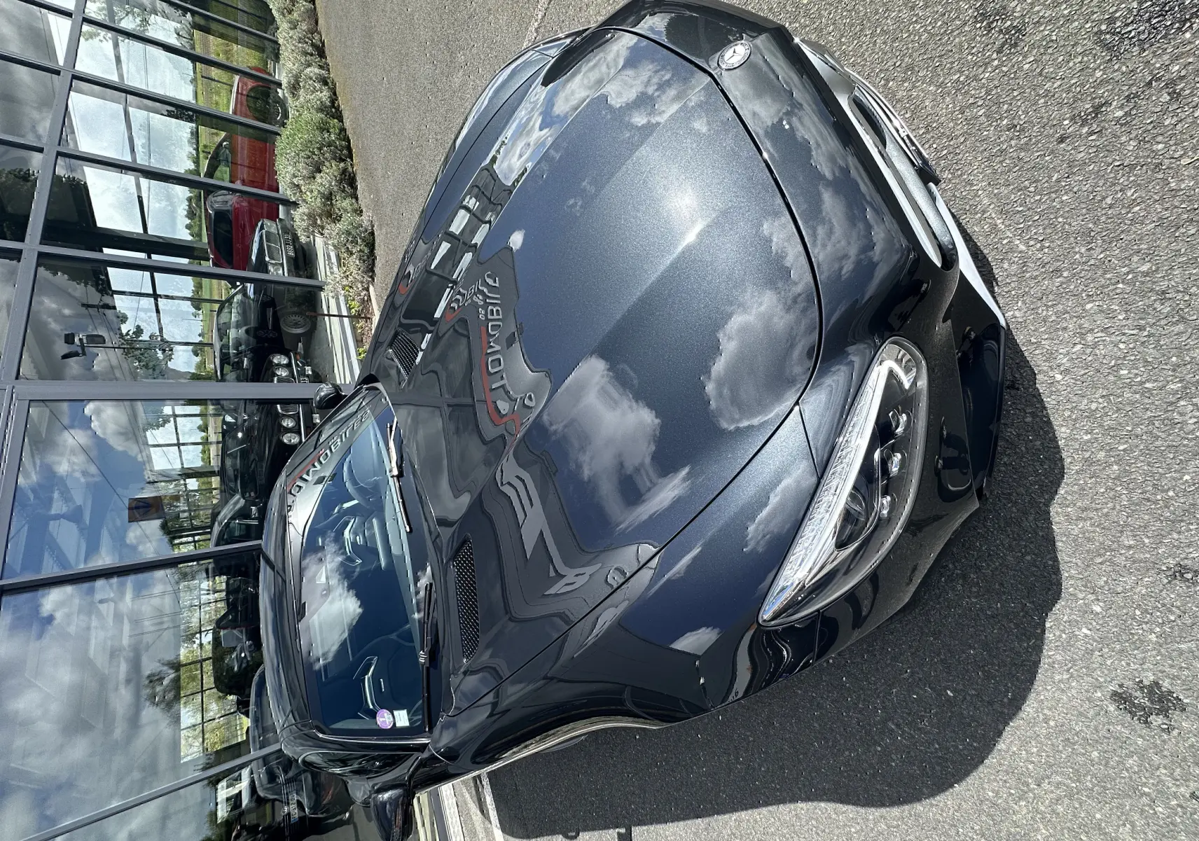 Vue 3/4 avant d'une Mercedes AMG GT gris foncé brillant, avec capot profilé et phares LED distinctifs.