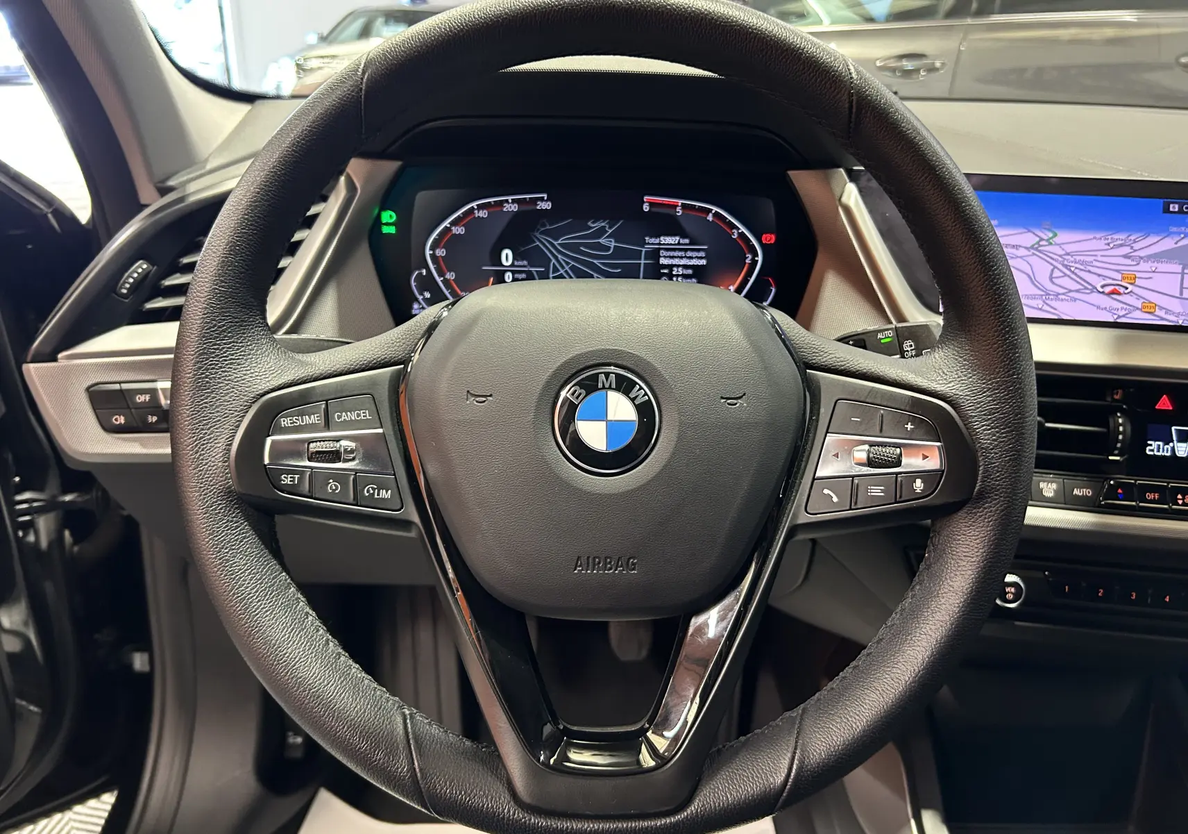 Vue rapprochée du volant noir d'une BMW Série 1 16d 2023 avec tableau de bord numérique et écran GPS intégré.
