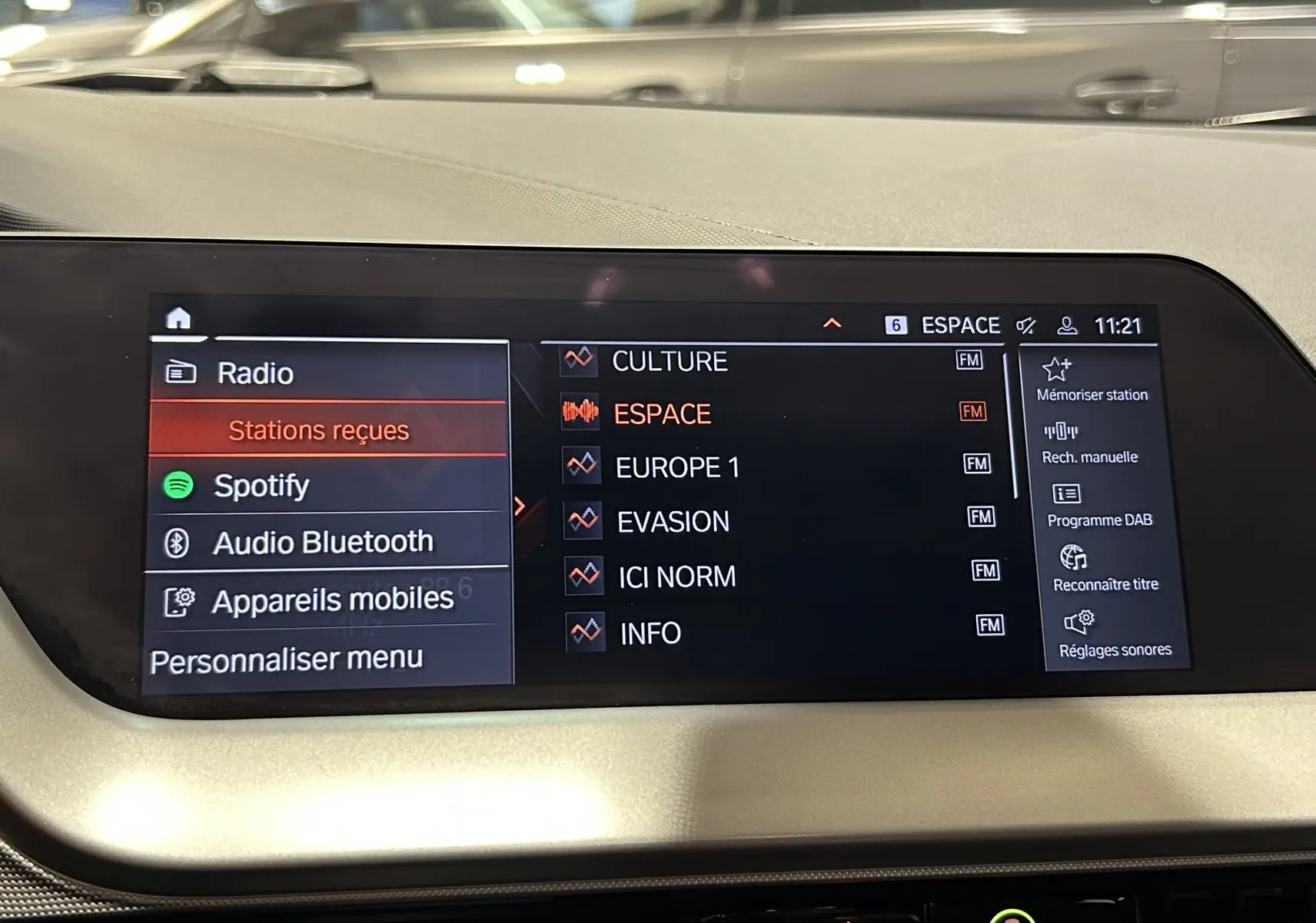 Écran central tactile de la BMW Série 1 16d 2023 affichant les options radio et Spotify dans un intérieur clair.