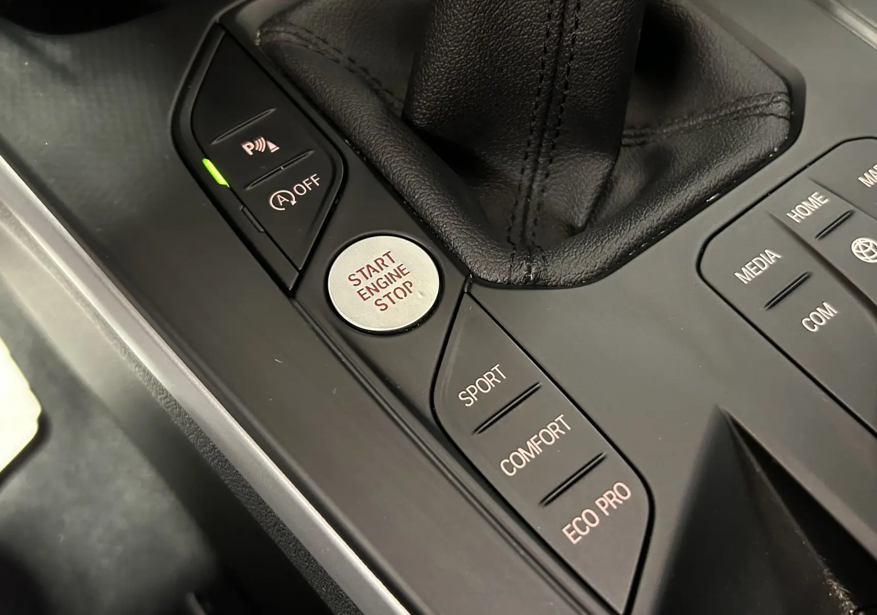 Gros plan sur la console centrale noire de la BMW Série 1 16d 2023, montrant les boutons de mode de conduite et le bouton Start Engine Stop.