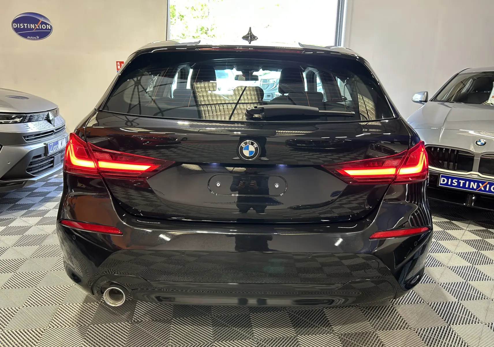 Vue arrière d'une BMW Série 1 noire de 2023 avec feux LED allumés dans un showroom intérieur.